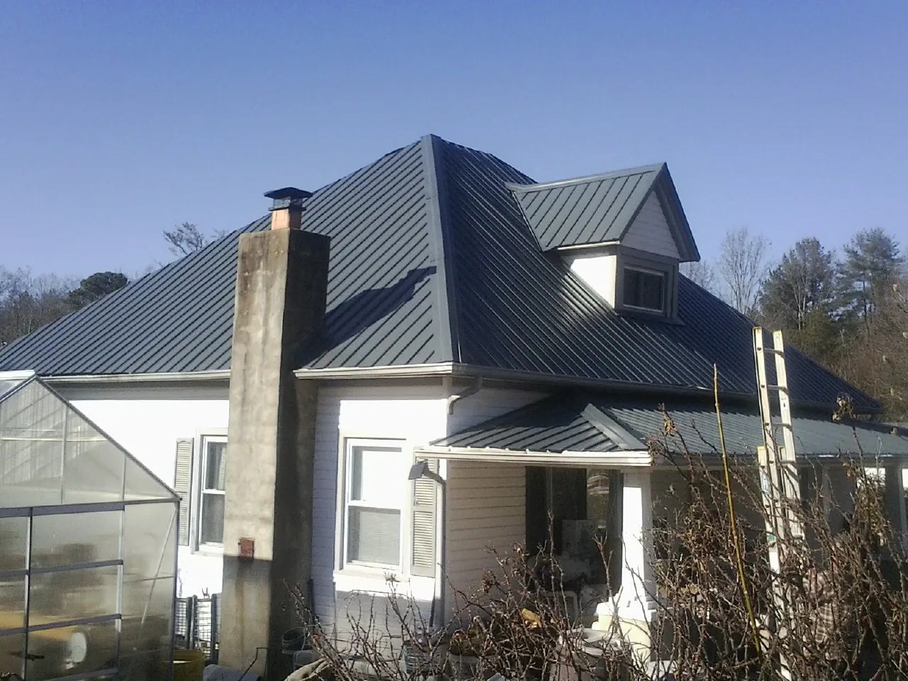 Dark blue standing seam metal roof on a white farmhouse with dormer — Slate & Tile Roof Repair by Roofing Brothers in Escalon