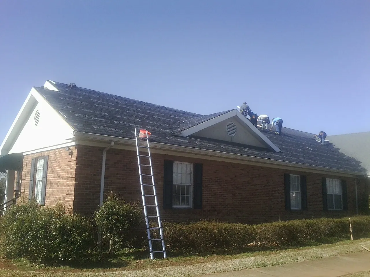 Crew tearing shingles off a brick ranch roof with a ladder set — Emergency Roof Repair work by our crew in Escalon