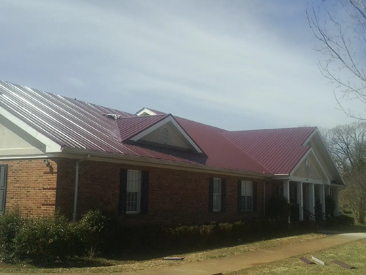 Red metal roof with gabled entries on a long brick building, from a Hail Damage Roof Repair job in Escalon