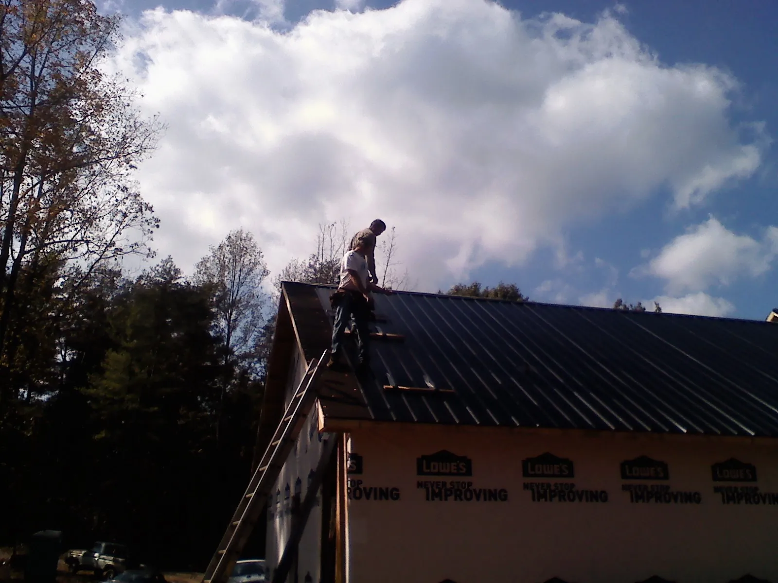 Roofer fastening dark metal panels high against a cloudy sky, from a Roof Inspection job in Escalon
